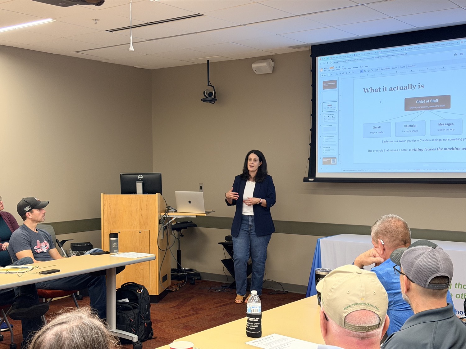 Shannon Owens speaking at AI Business Breakfast #8, explaining a diagram of an AI chief of staff routing work across Gmail, Calendar and Messages, to a seated audience at the REDI Office in Columbia, Missouri.